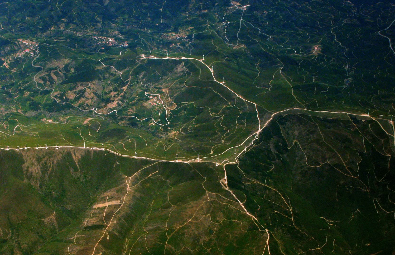 Aerial view of green hills crossed by roads, with a ridge of wind turbines